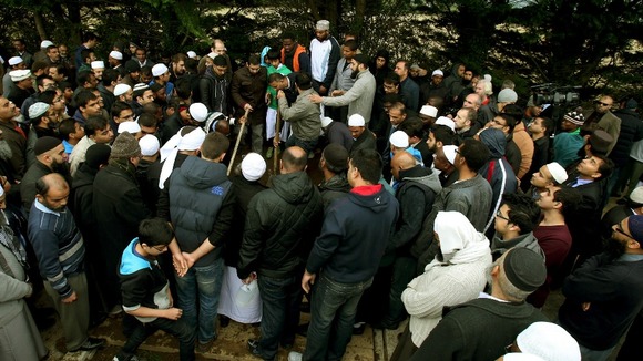 Mourners stand over a grave at the burial of members of the Al Sattar family, who died in a suspect arson attack in Leicester