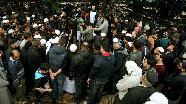 Mourners stand over a grave at the burial of members of the Al Sattar family, who died in a suspect arson attack in Leicester