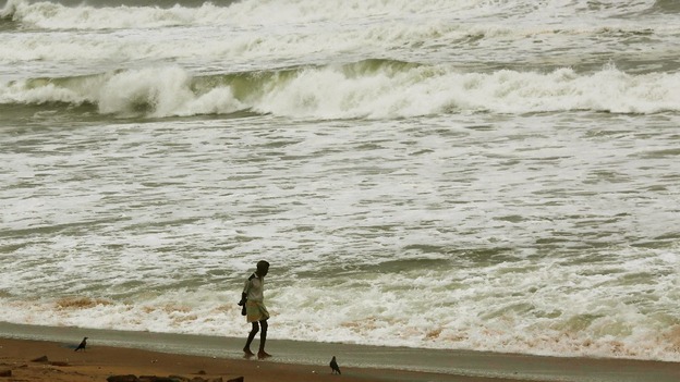 A man walks as waves from the Bay of Bengal approach the shore.