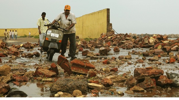 People walk among debris from a broken wall after it was damaged by a wave brought by Cyclone Phailin.