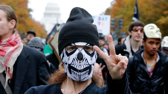 A supporter of the Anonymous movement gestures as she marches with a crowd of protesters with the US Capitol in the background.