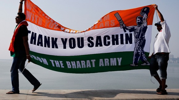 Cricket fans walk on a sea wall while holding a banner thanking cricketer Sachin Tendulkar.
