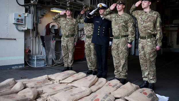 Members of the UK and Belgium military salute in front of the sacred soil aboard the Belgian Frigate Louise Marie.