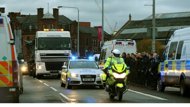 Police officers line the street as the wreckage of the police three-tonne Eurocopter is taken away