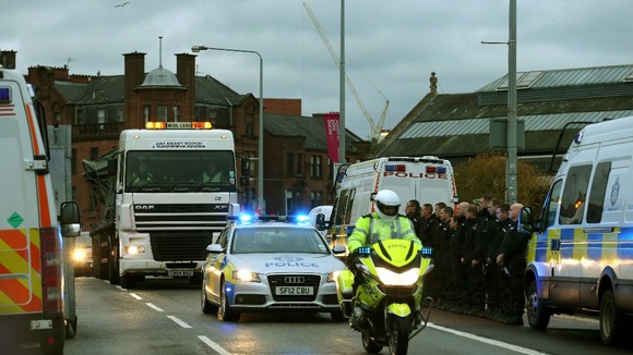 Police officers line the street as the wreckage of the police helicopter is taken away by lorry