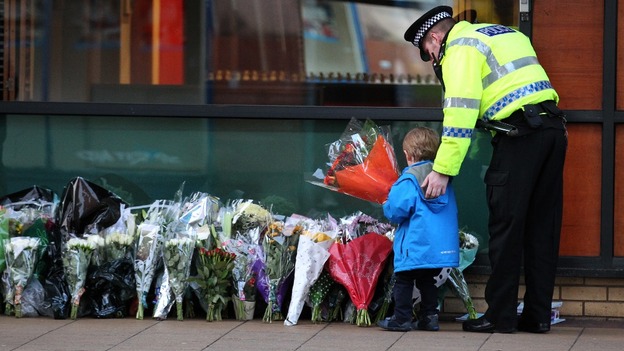 A police officer escorts a child laying flowers for the victims of the Glasgow helicopter crash