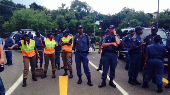 Police line the street in Pretoria where a crowd has gathered.