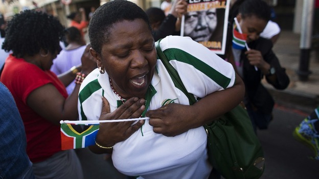 Women sing and dance as the hearse drives past them.