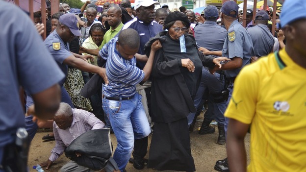 A man falls to the ground as mourners push through the metal gates in Pretoria.