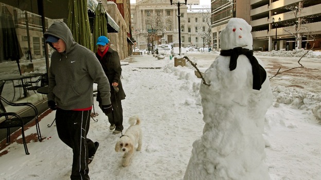 A couple walks their dog past a snowman near the State Capitol building in Indianapolis, Indiana