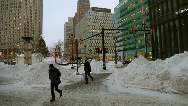 Pedestrians walk past mounds of snow during bitter cold temperatures in downtown Detroit, Michigan