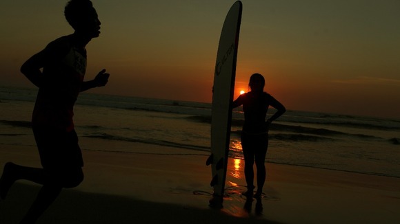A man jogs as a surfer stands with a surfboard during sunset at Kuta beach, on the resort island of Bali