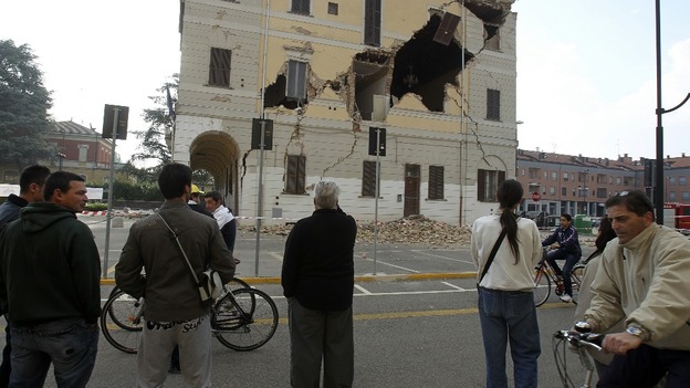People gather on a street in front of the damaged Town Hall building