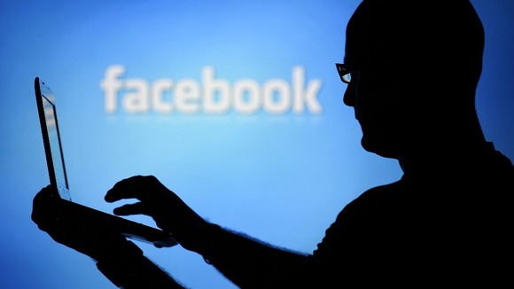 A man is silhouetted against a video screen with an Facebook logo