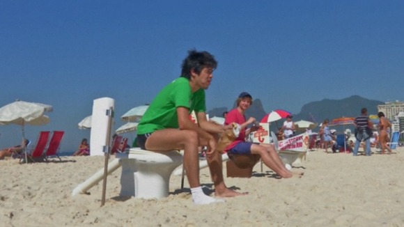 A protester eats his lunch on a toilet on the beach.