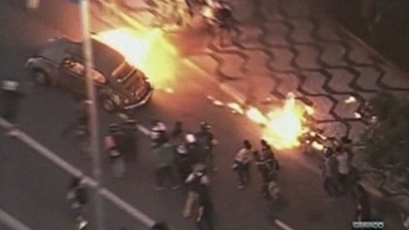 A burning car is driven through the streets.