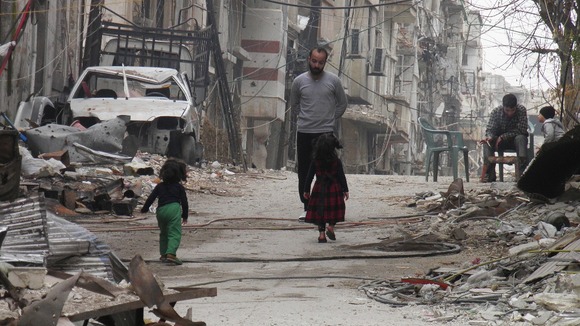 Civilians stand along a street lined with rubble in the besieged area of Homs