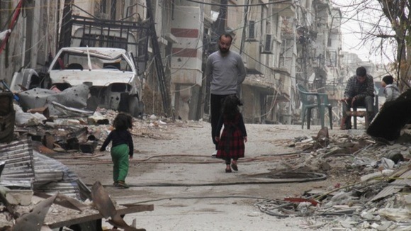 Civilians stand along a street lined with rubble in the besieged area of Homs.
