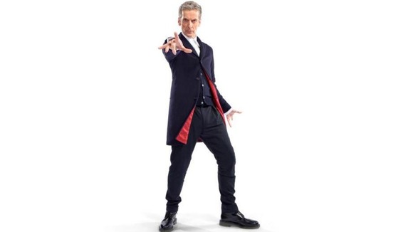 Peter Capaldi wearing a dark blue Crombie coat with red lining, dark blue trousers, a white shirt and Doc Martins.