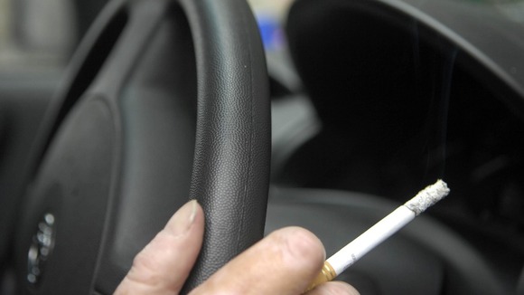 A man holds a cigarette while at the wheel of a car.