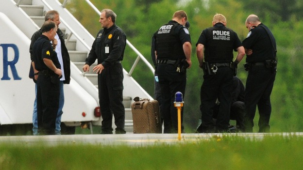 Law enforcement officials stand near a jet bridge next to the passenger jet on the tarmac 