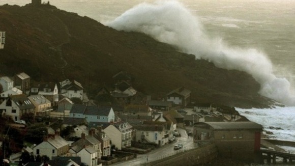 A wave breaks over a headland in Sennen Cove near Land's End