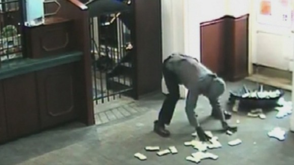 The suspect frantically tries to put all the money into an open umbrella.