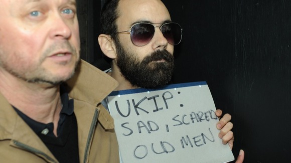 A man (right) is restrained after throwing an egg at Nigel Farage.