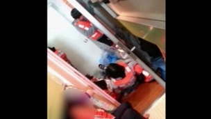 Students wearing life jackets are seen lying on the floor.