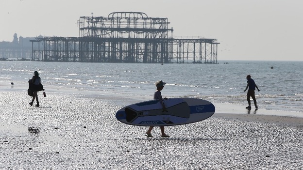 A woman carrying a paddle board across Hove beach, East Sussex.