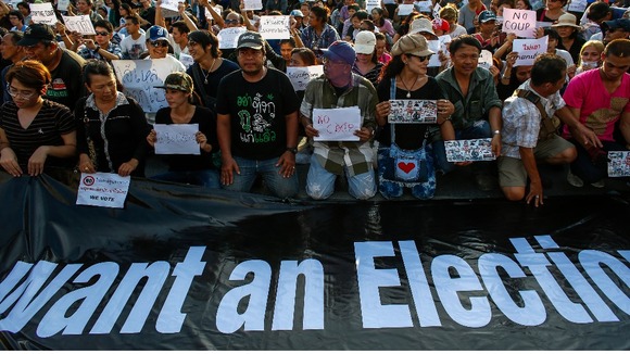 People hold signs while kneeling during a protest against military rule at Victory Monument in central Bangkok.