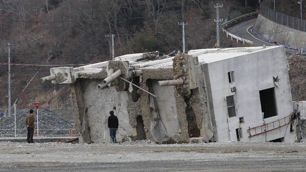 Visitors look at a fallen building in the neighborhood destroyed by the tsunami