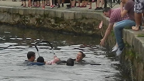 A baby who fell into a river after her pram rolled off a quayside was saved by a passing rowing team.