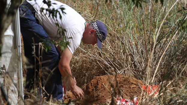 A British police officer checks soil samples dug from a hole in an area of wasteland
