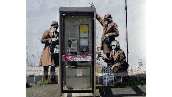 The graffiti depicts figures in sunglasses and trench coats listening in on calls
