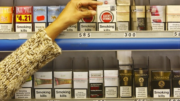 A person grabs cigarettes from a shop shelf.