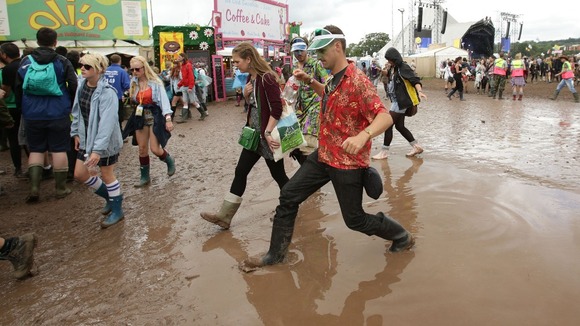 Festival goers manoeuvre through a puddle of mud at the Glastonbury Festival today.