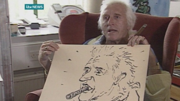 Jimmy Savile poses with the portrait Rolf Harris drew of him.