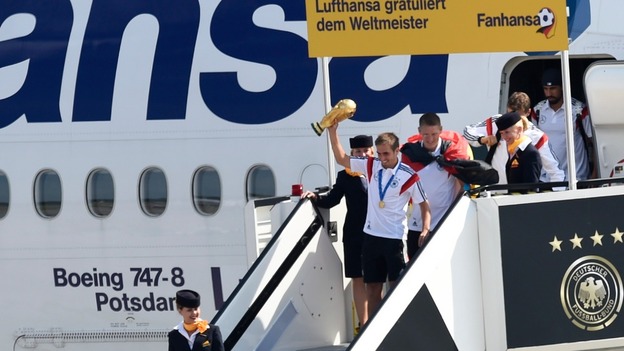 Captain Philipp Lahm holds the trophy aloft as the side leave the plane.