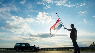 A Netherlands flag flying at half-mast as a hearse carrying victims passes.