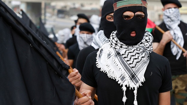Refugees, wearing Palestinian traditional headscarves and carrying black flags, attend a demonstration calling for an end to the Israeli offensive.