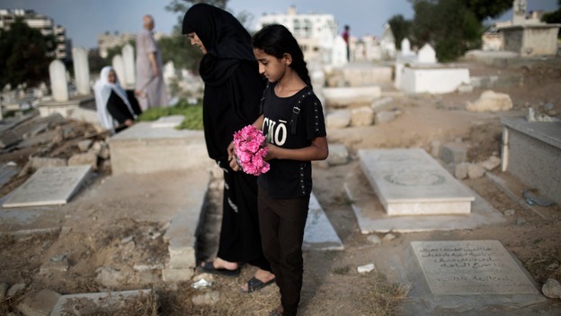 A woman and girl carry flowers to a family grave.