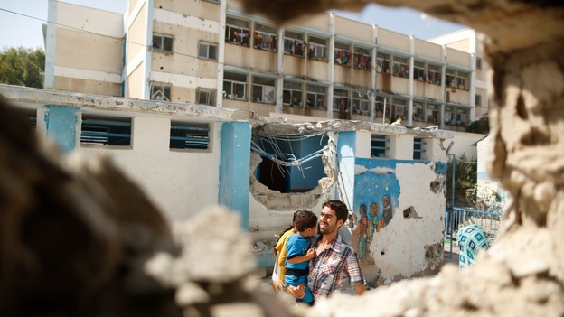 A man carries a child through the remains of a classroom being used as a UN shelter in Gaza.