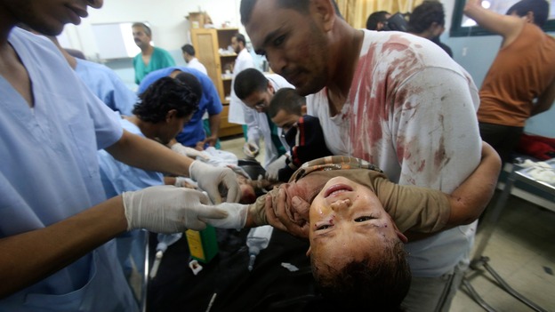 A man holds his young son to be treated by medics in a hospital in Khan Younis