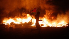 A Palestinian protester holds a flag as he runs past burning tyres during clashes with Israeli troops.