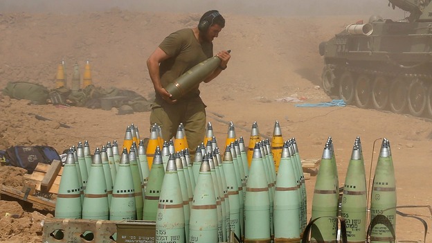 An Israeli soldier carries a shell at a mobile artillery unit as it fires on the Gaza Strip.
