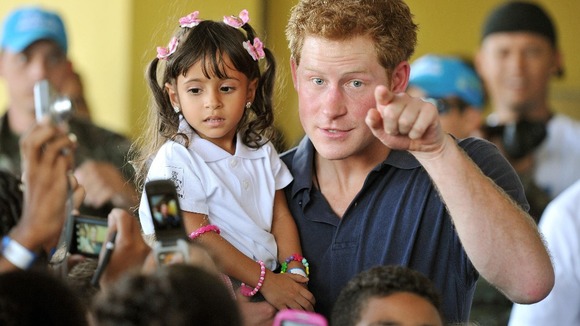 Prince Harry speaks to young children as he holds Mayara Pereira, 3, in his arms, during a visit to the Favella of Complexo do Alemao