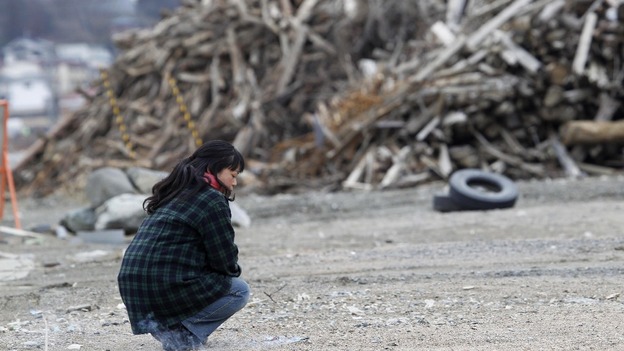 A woman kneels near a pile of debris while offering prayers in the devastated city of Rikuzentakata
