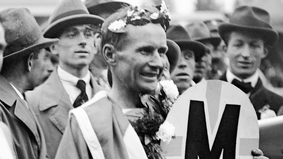 Hannes Kolehmainen of Finland draped in the Finnish flag and crowned with a wreath of laurels after winning the Marathon in 1920