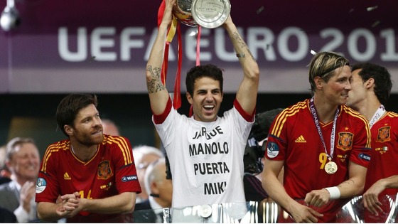 Spain midfielder Cesc Fabregas lifts a trophy wearing a t-shirt honouring the deaths of Spanish footballers and Manolo Preciado.